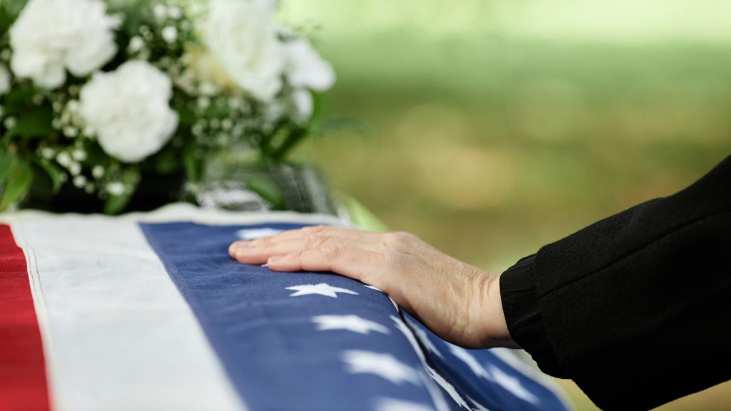 Surviving spouse with casket and American flag