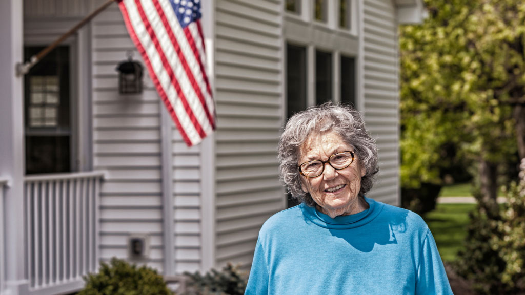 Elderly woman in front of American flag house