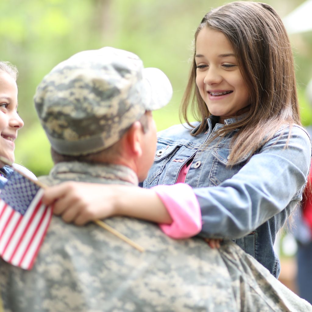 Child holding an American flag while embracing a person in military uniform