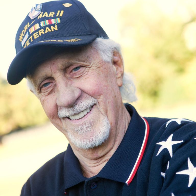Smiling older man wearing a World War II veteran cap and a star-patterned shirt