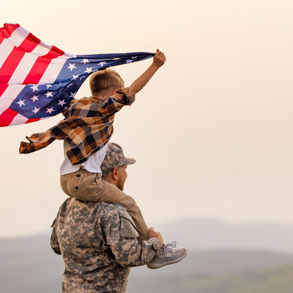 Person in military uniform carrying a child holding an American flag